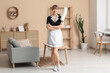 © Pixel-Shot - Smiling maid with hand duster in living room