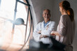 © Westend61 - Smiling senior doctor talking to woman at the window in medical practice