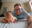 © phpetrunina14 - Playful father and baby selfie on bed at home.