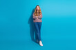 © deagreez - Young stylish woman in blue studio wearing sweater and jeans smiles confidently against blue background for lifestyle fashion concept