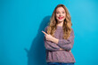 © deagreez - Young woman in a cozy sweater points to the left with a bright smile against a blue background conveying casual fashion style and a friendly lifestyle