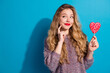 © deagreez - Young stylish woman with a heart shaped lollipop smiles against a blue background promoting fashion style chic glamour and playful joy in a casual winter scene