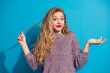 © deagreez - Young stylish woman with blonde hair wearing a purple sweater posing against a blue background