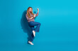 © deagreez - Young woman jumps with phone in hand exuding joy fashion and energy against blue background