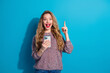 © deagreez - Young woman with phone smiles brightly and points up against blue background suitable for lifestyle shopping promotion and social media campaigns