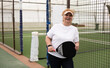 © Angelov - Portrait of senior woman playing padel on outdoor court, ready to hit ball. Health and active lifestyle concept.