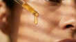 © Yash - Woman applying face oil with glass dropper on freckled cheek