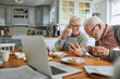 © Marko Geber - Smiling senior couple using smartphone at breakfast in home kitchen
