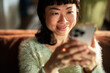 © Davor - Smiling woman using smartphone on couch at home
