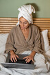 © sutulastock - Woman working on laptop in bed at home wearing bathrobe and towel enjoying calm morning indoors remote work wellness lifestyle comfort relaxation productivity