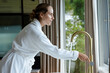 © Wavebreak Media - Woman in her 20s wearing white robe at kitchen sink operating brass gooseneck faucet, water flowing