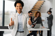 © Novak - Successful African American businesswoman showing thumbs up with colleagues in background