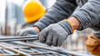 © Nataliya - Faceless construction worker's hands tying rebar, close-up gloved hands securing, metal rods building infrastructure, precision care construction detail, with copy space