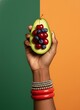 © DesignBuzz - Hand holding a halved avocado filled with cherries and blueberries against vibrant background