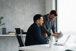 © Novak - Two professional male colleagues having a meeting and looking at a laptop in a bright workspace