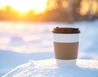© Chan - Paper cup of coffee/tea sits atop a snow-covered surface during golden hour, blurred trees in the distance