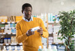 © JackF - Focused African American in casual ochre jumper and glasses examining healing ointment box in pharmacy, checking instructions before using for wounds or burns
