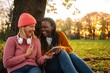 © Jelena - Friends laughing looking at smartphone in autumn park