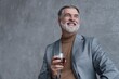© opolja - Confident mature businessman chilling relaxing drinking enjoying whiskey against grey wall.
