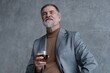© opolja - Confident mature businessman chilling relaxing drinking enjoying whiskey against grey wall.