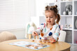 © New Africa - Cute little girl playing with toys at wooden table indoors