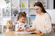 © New Africa - Mother and her daughter playing with toys at wooden table indoors