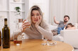 © New Africa - Alcohol addiction. Woman drinking whiskey at wooden table while her scared husband and daughter sitting on sofa indoors, selective focus