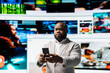 © DC Studio - User engages with multimedia content on smartphone, sending likes across social networks. African american man browses dashboard of streaming videos and social media feeds on digital wall