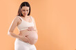 © New Africa - Pregnant woman touching her belly on orange background, space for text