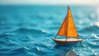 © miss irine - Small wooden sailboat with orange sail floats on bright blue wavy sea. Close up view of miniature toy boat drifting on clear ocean water surface under sunny sky.
