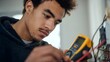 © FrameLab - Young Apprentice Electrician Learning To Use Multimeter For Voltage Testing In Training