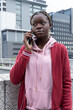 © wavebreak3 - African American teen standing on overpass holding phone to ear beside concrete wall maroon jacket