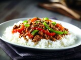 Asian style ground chicken over steamed rice with vegetables and glossy sauce on white plate