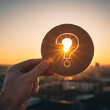 © Jim - Hand holding wooden question mark symbol against sunrise sky for future business vision, financial uncertainty, new opportunity, strategic thinking unpredictable economic forecast concept. Business