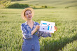 © sofiko14 - A smiling woman in overalls and a straw hat stands in a green field, holding a paper with a growing bar chart and arrow