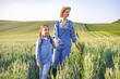 © sofiko14 - A mother and her young daughter walk hand-in-hand through a lush green wheat field under a clear sky, embodying a sense of rural life and family connection