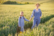 © sofiko14 - A mother and her young daughter hold hands while walking through a golden wheat field at sunset, embodying a sense of family and rural life