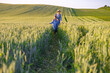 © sofiko14 - A mother and her daughter walk through a lush green wheat field under a clear sky, enjoying a sunny day together