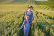 © sofiko14 - A mother and her young daughter walk through a lush green wheat field under a bright sky, enjoying a moment of connection and nature