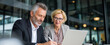 © ray - Two partners team of professional business people working discussing writing notes at desk. Mature teacher mentor leader man showing young woman manager project on laptop in office. Banner, copy space