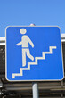 © nahhan - A square blue traffic sign with a white silhouette of a person walking down a set of stairs indicates an underground pedestrian crossing against a clear sky