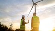 © DawDunia - At sunset on a wind farm, engineers wearing safety vests work together to examine wind turbines, strategizing for sustainable energy growth and overseeing performance