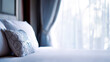 © Small - Hotel bed with crisp white linens and decorative pillow in soft morning light through sheer curtains.