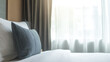 © Small - Hotel bed with crisp white linens and decorative pillow in soft morning light through sheer curtains.