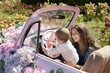 © Anna - young mother and her little daughter are having a fun time sitting in an old pink car decorated with flowers in a park on a sunny summer day. Walks together, weekends with family, enjoying the moment