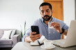 © kleberpicui - Man working from home using laptop and smartphone while drinking water, representing remote work, productivity and modern digital lifestyle.