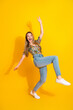 © deagreez - Young woman jumping in bright yellow studio wearing floral top jeans and sneakers enjoying fashion lifestyle