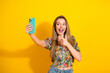 © deagreez - Young woman takes a cheerful selfie against a vibrant yellow background in a floral top