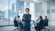 © zalifx - Confident businesswoman in a modern office meeting room with a city skyline view, colleagues in the background.