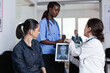 © DC Studio - Medical staff female members attending sick young woman in hospital lobby. African american nurse assisting doctor in consultation at medical clinic. Physician giving patient test results.